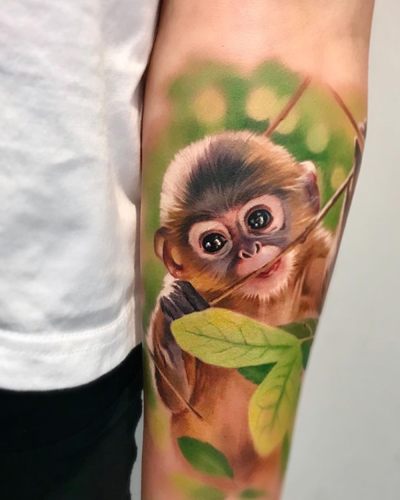 Full colour realism tattoo of a young monkey holding a leaf
