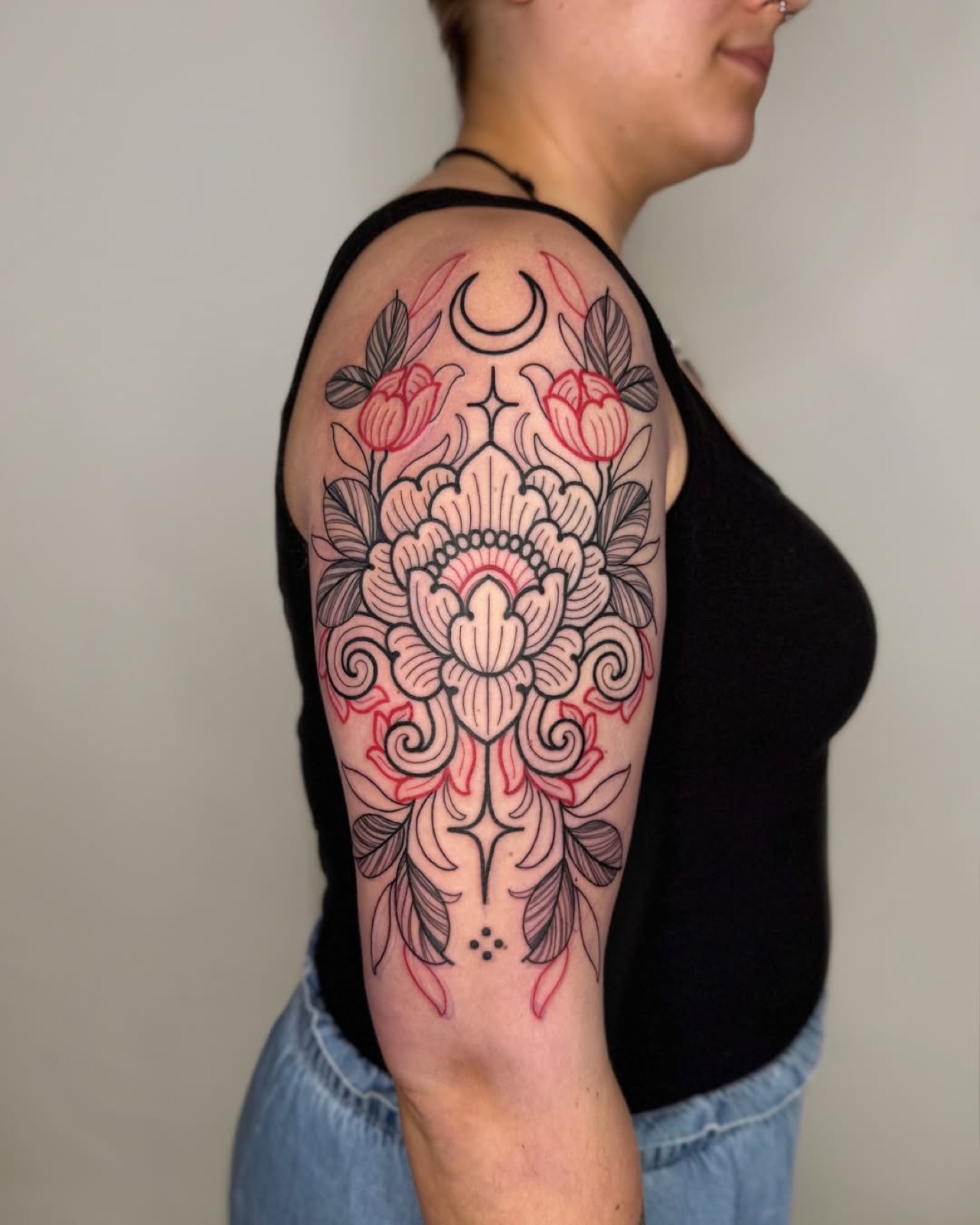 Ornamental floral upper arm tattoo in black linework with red accents