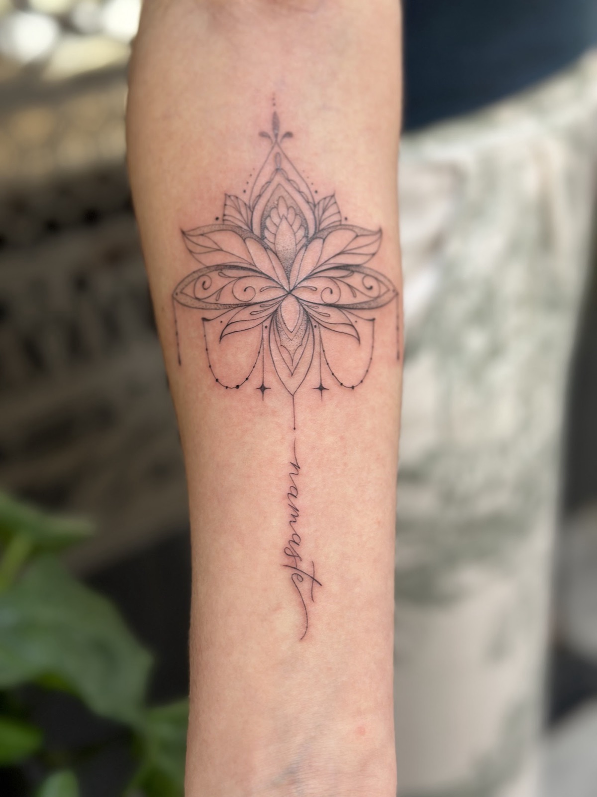 Fine line ornamental lotus forearm tattoo with fine script beneath it